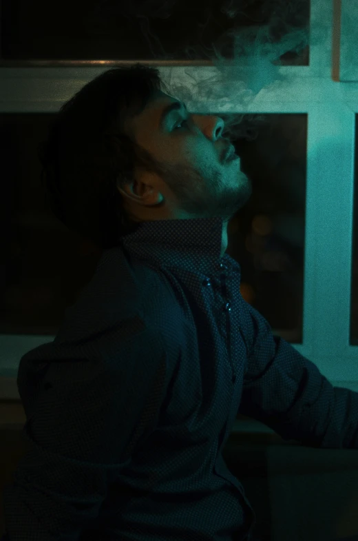 a man is smoking cigarette while sitting next to a window