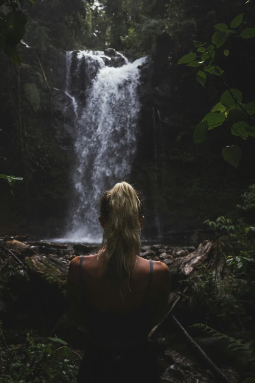 woman at the base of waterfall looking at waterfall