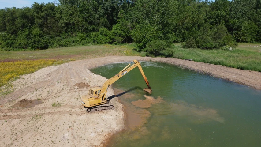 a bulldozer moving gravel across water into a large pond