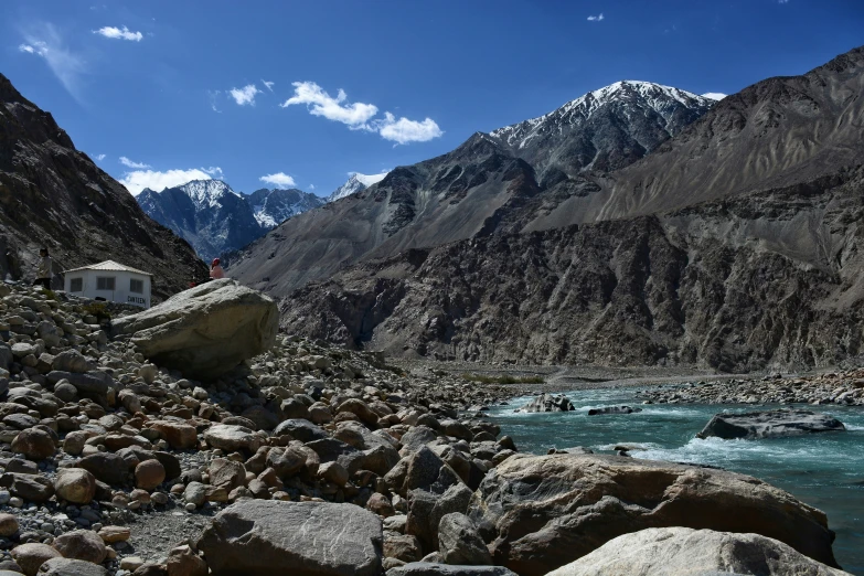 a small hut next to a river in front of mountains