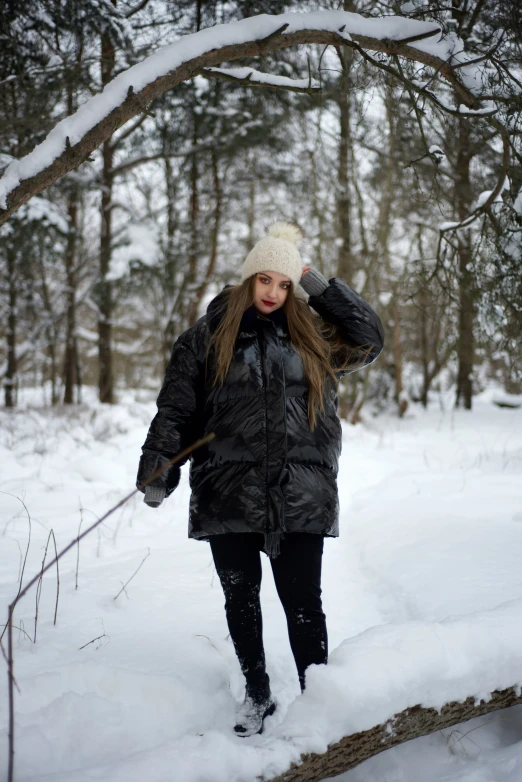 a woman in black coat walking through snowy forest