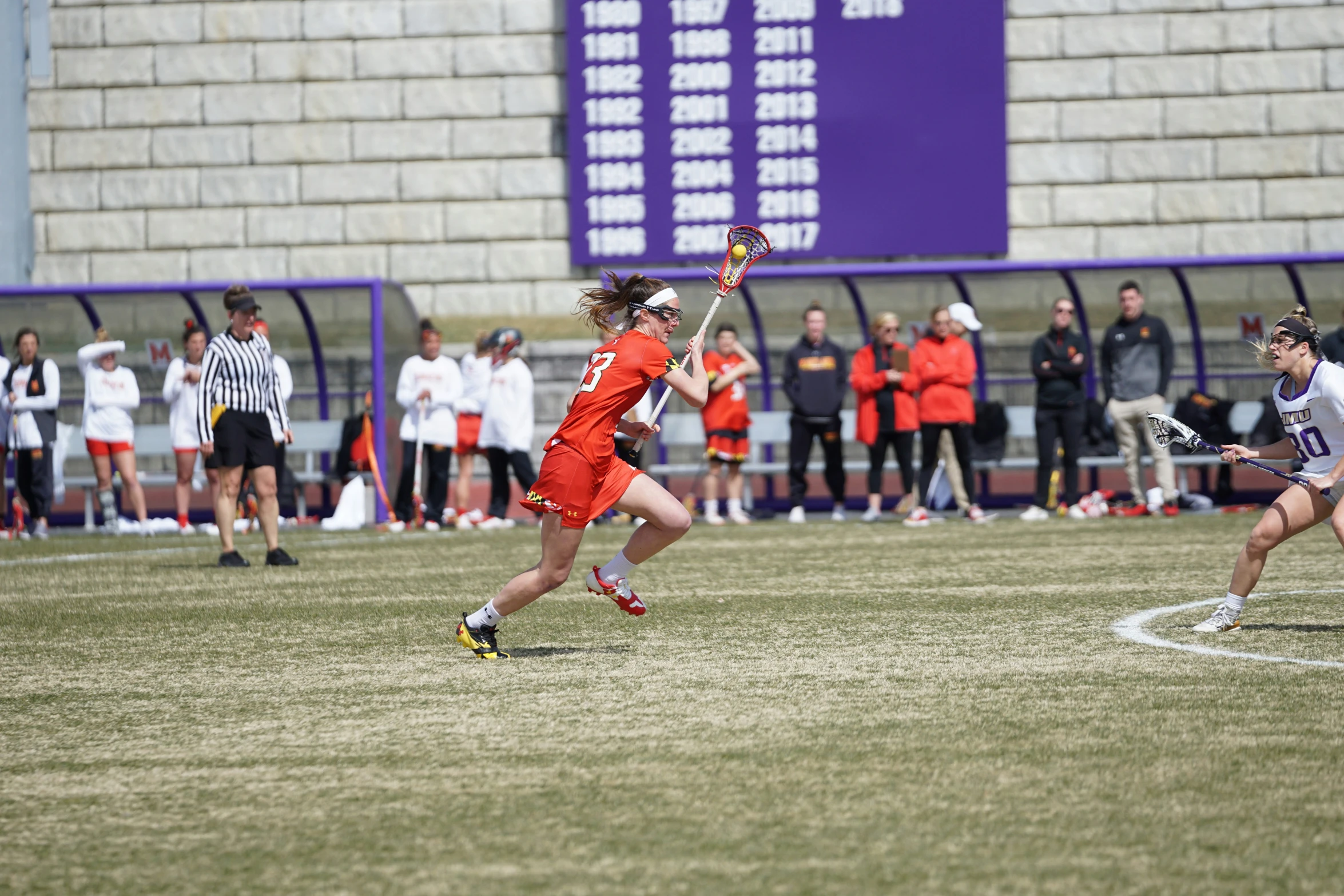 two girls playing lacrosse while a crowd watches