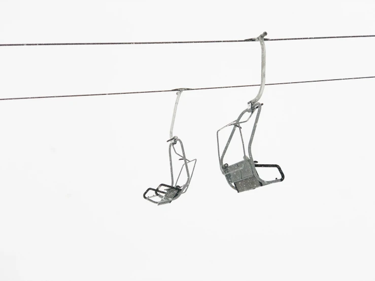 two empty seats suspended from wires in the snow