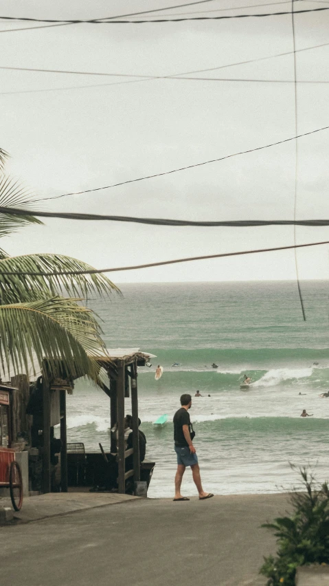 a man walks near a hut with surfboard in the background