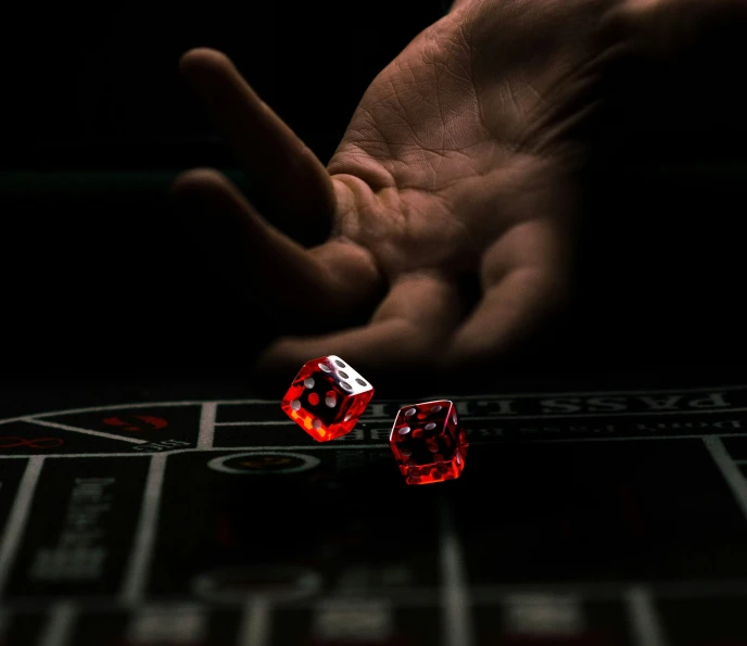 a hand holding two dice over a roule with one hand behind it