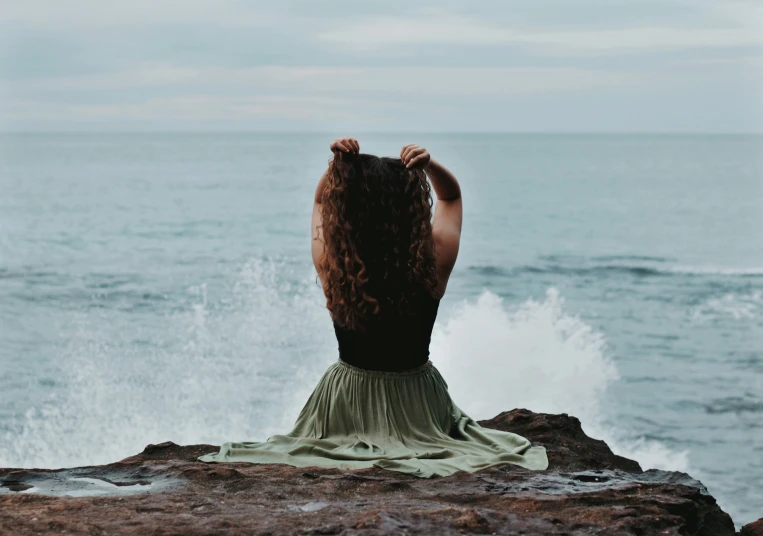 a woman with long hair standing on top of a rock near the ocean