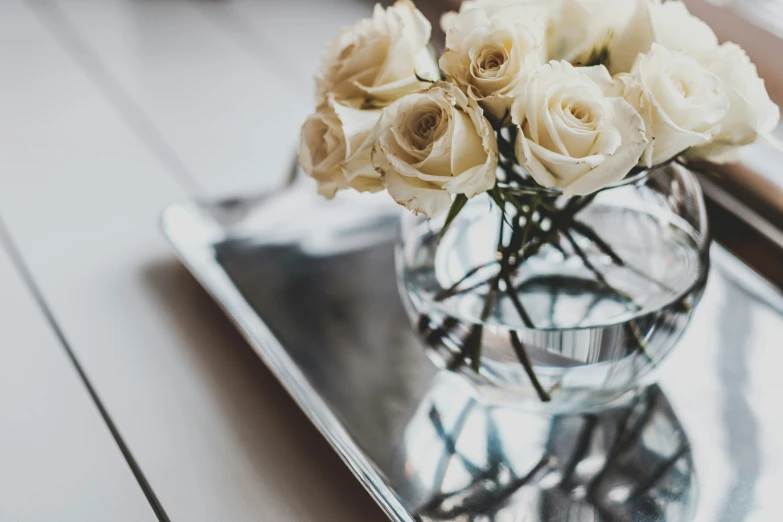 a vase with white roses on a glass tray