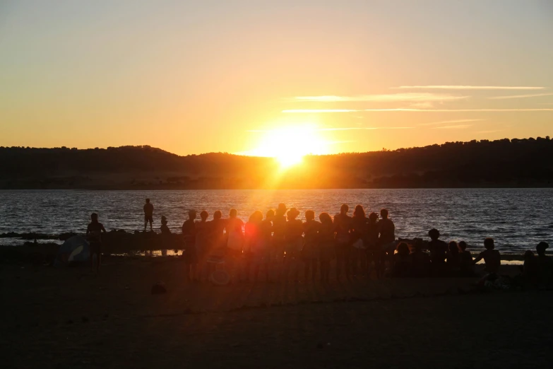 a bunch of people gathered on the beach for a sunset party