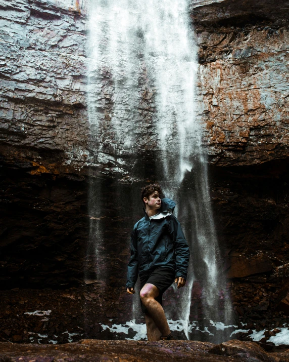 man with black jacket standing in front of a waterfall