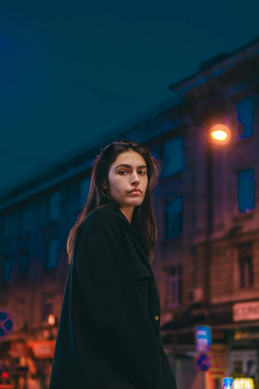 a woman is standing on a city sidewalk with the lights on