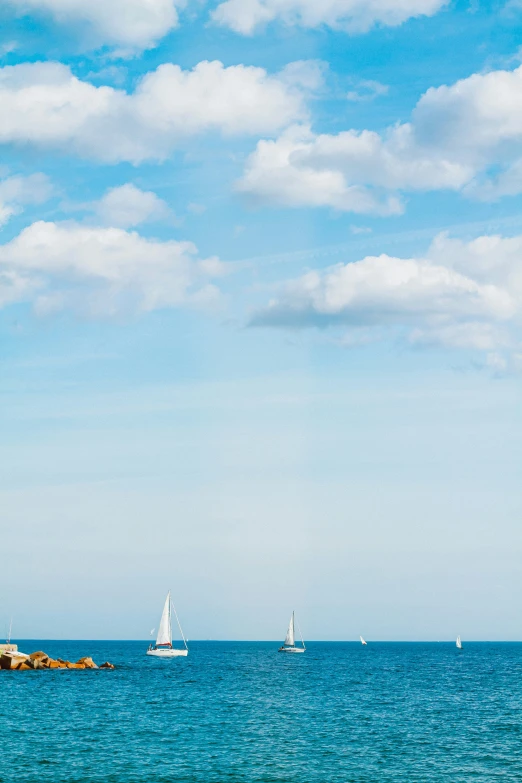 sailboats sailing on the ocean under a cloudy blue sky