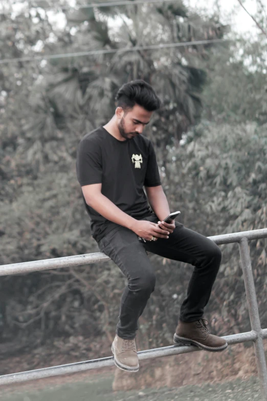 a man sitting on a fence using his cell phone