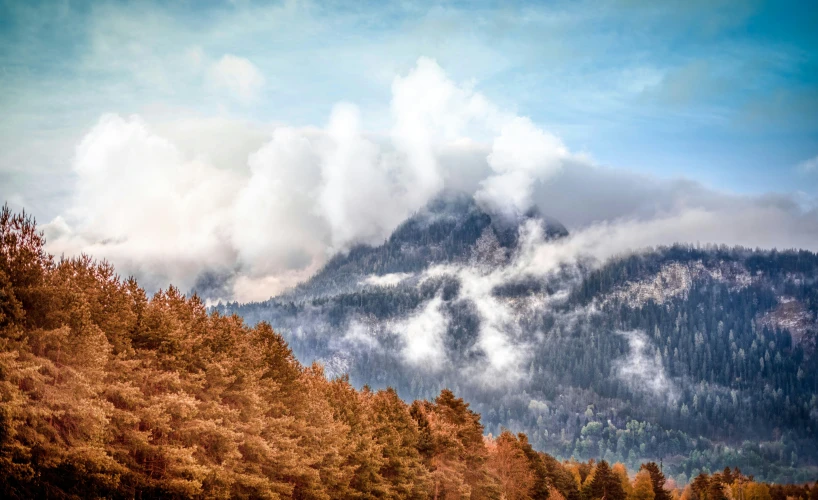 clouds coming from a high mountain range with trees below