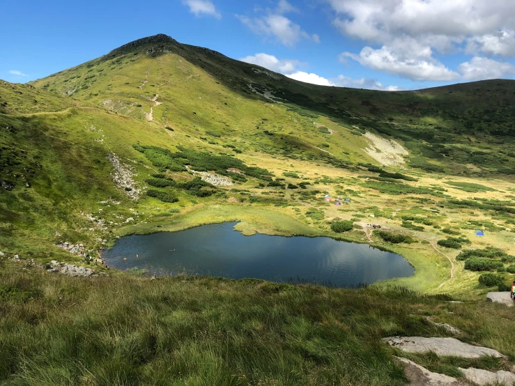 a lake on the side of a green mountain