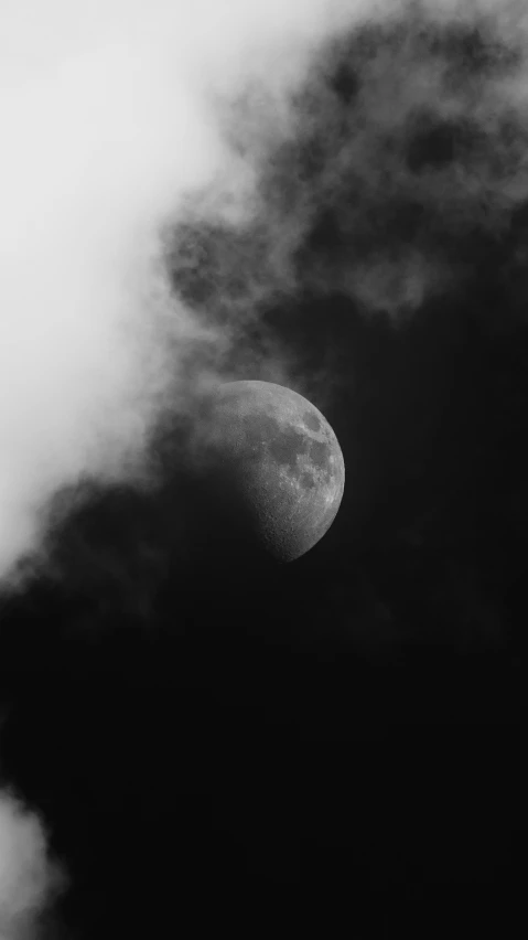 a half moon partially obscured in clouds, under a dark sky