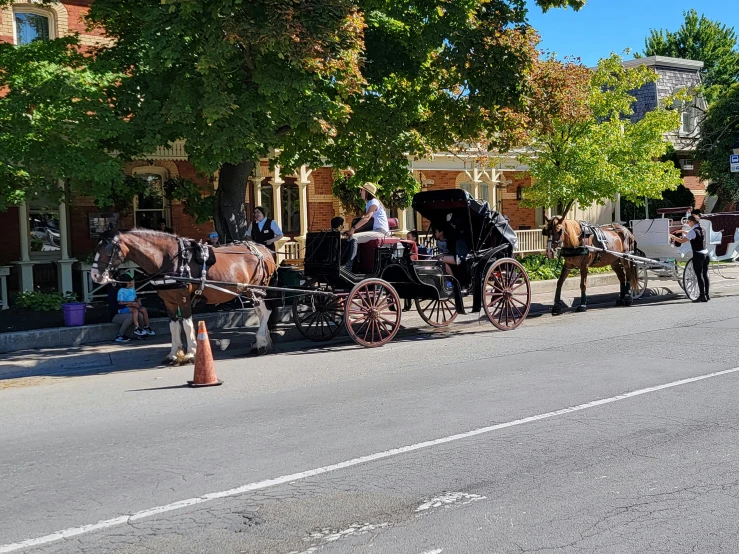 people stand on the side of a street as horses and carriages pull in front