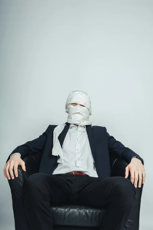 a man with a mask sitting on top of a black chair