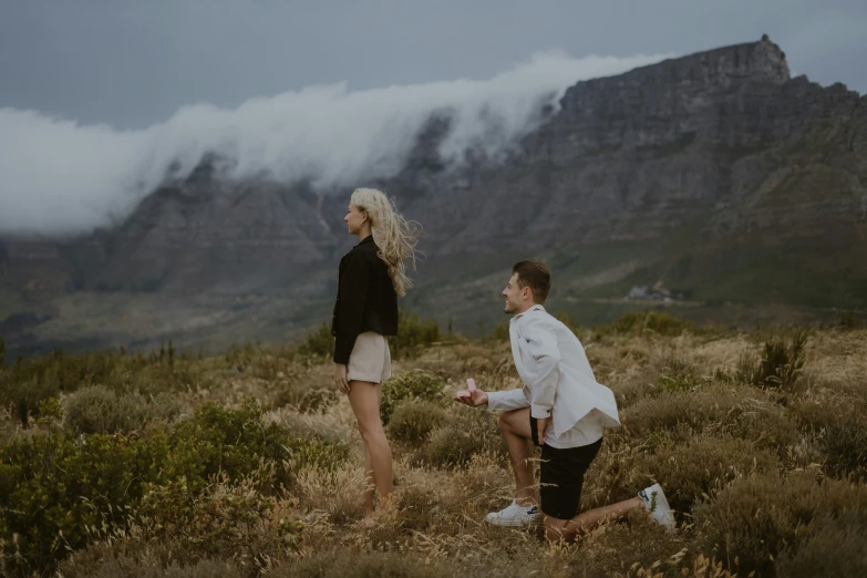 two men standing in a grass field with mountains behind them