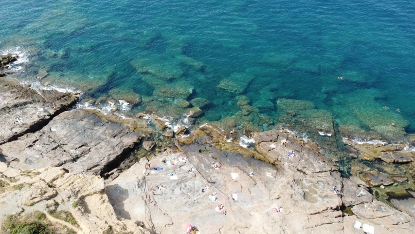 view of water from the air, including small groups of rocks and people on beach below