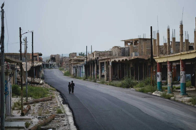 two people walking on a deserted street near dilapidated buildings