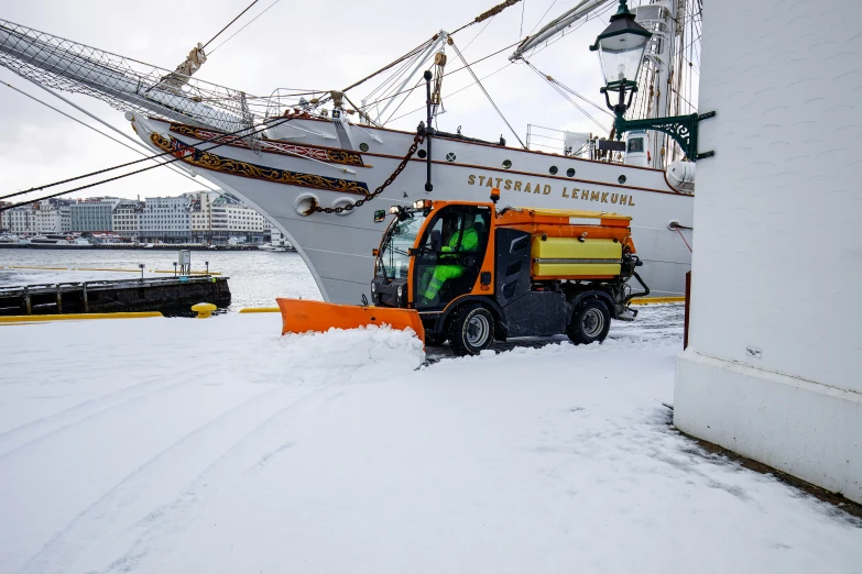 a tractor with snow grooming in front of a large ship