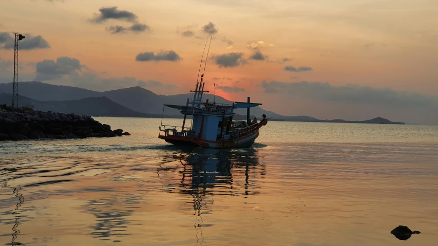 a fishing boat floats on the water as the sun sets