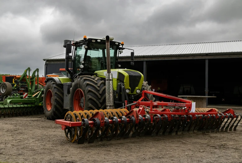 two tractors and two equipment parked near a barn