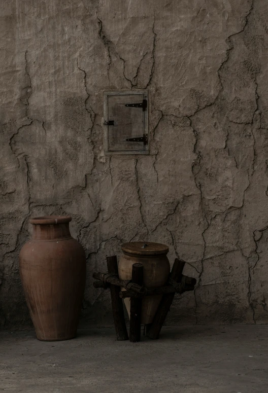 two jars stand on the ground next to a concrete wall