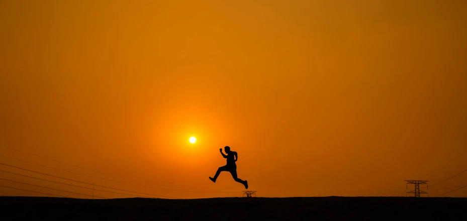 the silhouette of a man is running as the sun sets