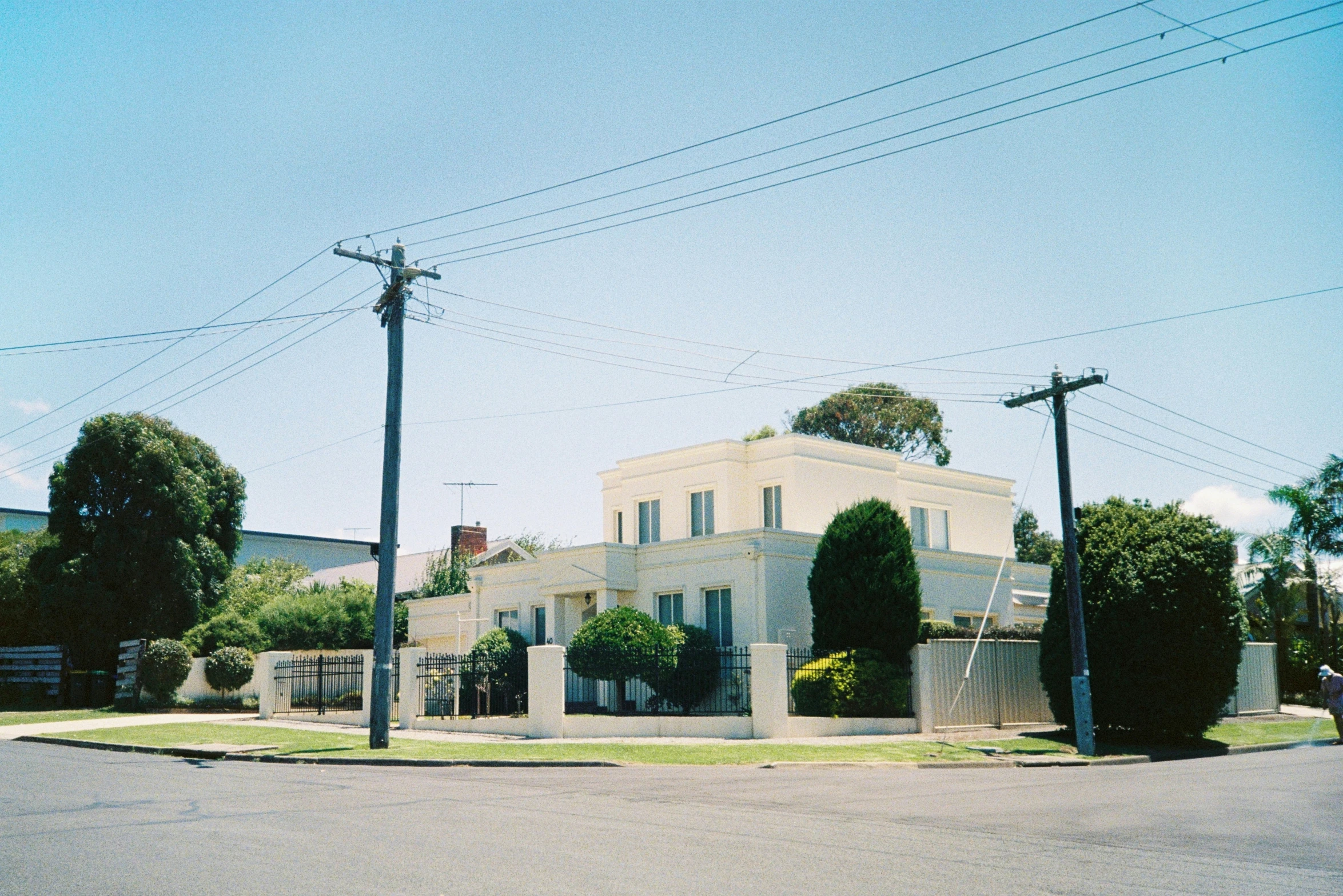 an intersection with three telephone poles and a large house on the side