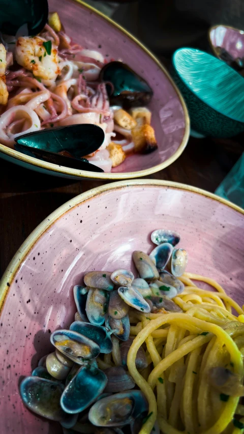 a bowl filled with noodles and clams, while another bowl filled with shrimp are sitting on the table