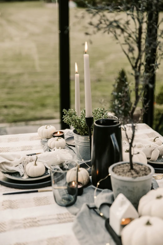 a table with a black and white tablecloth covered in white pumpkins and a can of candles next to it