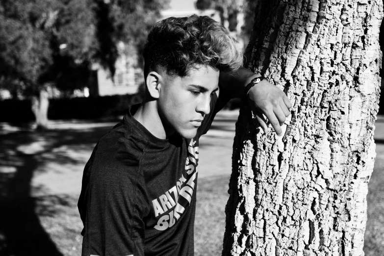 a boy is leaning against the tree looking at soing