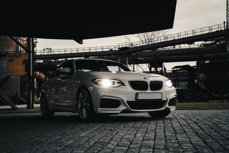 a grey car parked on cobblestone surface in front of a factory