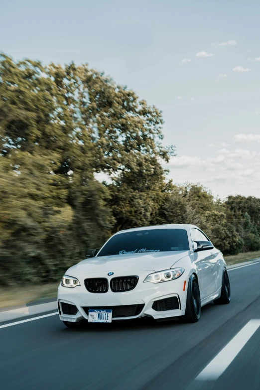 a white car driving down a road next to trees