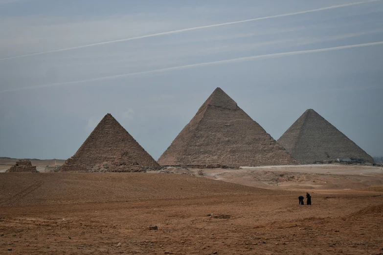 a group of three pyramids are standing on some desert