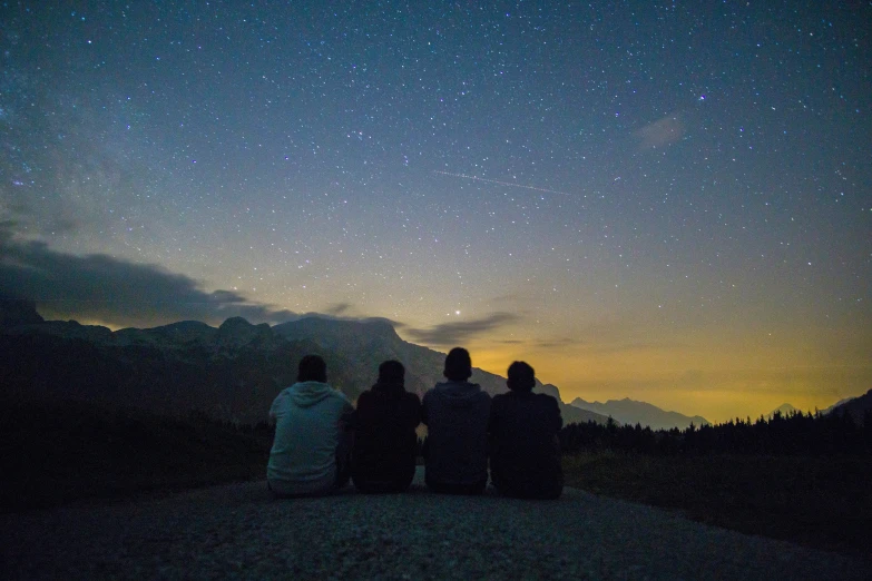 a group of people sitting on top of a hillside watching the stars