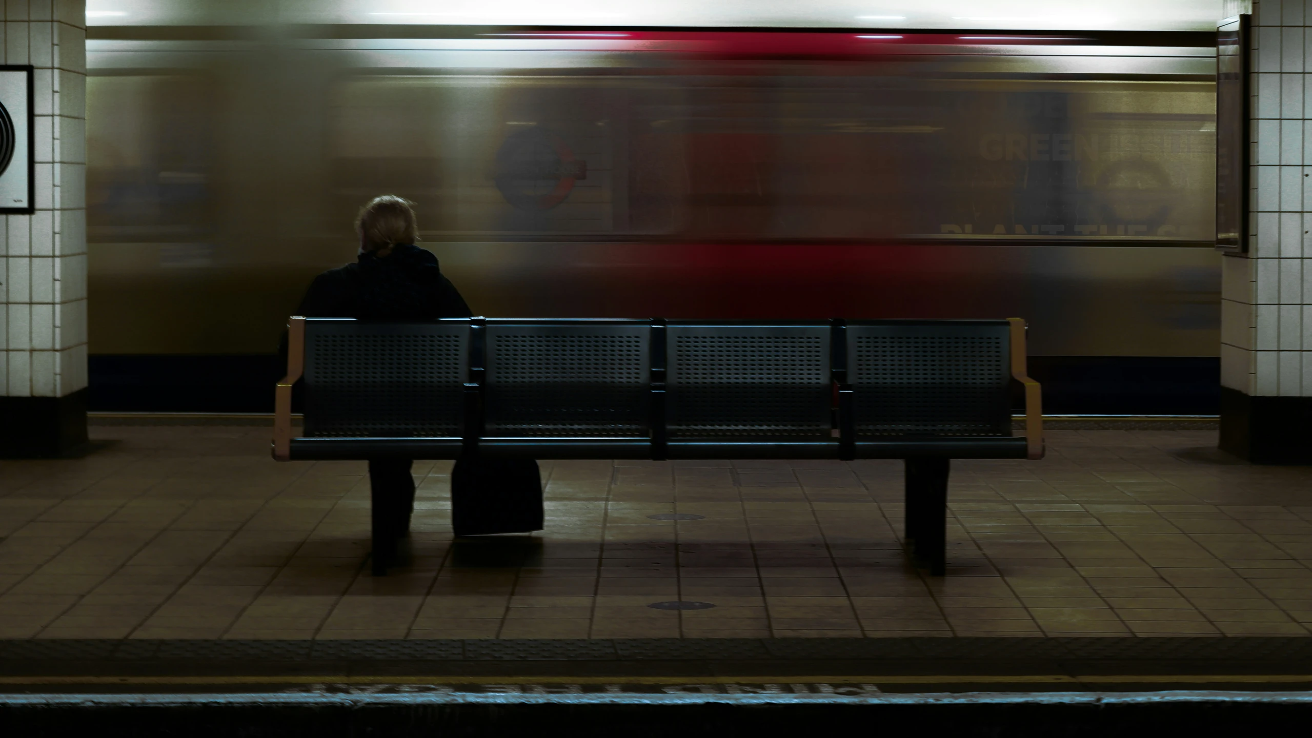 a woman is sitting on a bench as a train speeds by