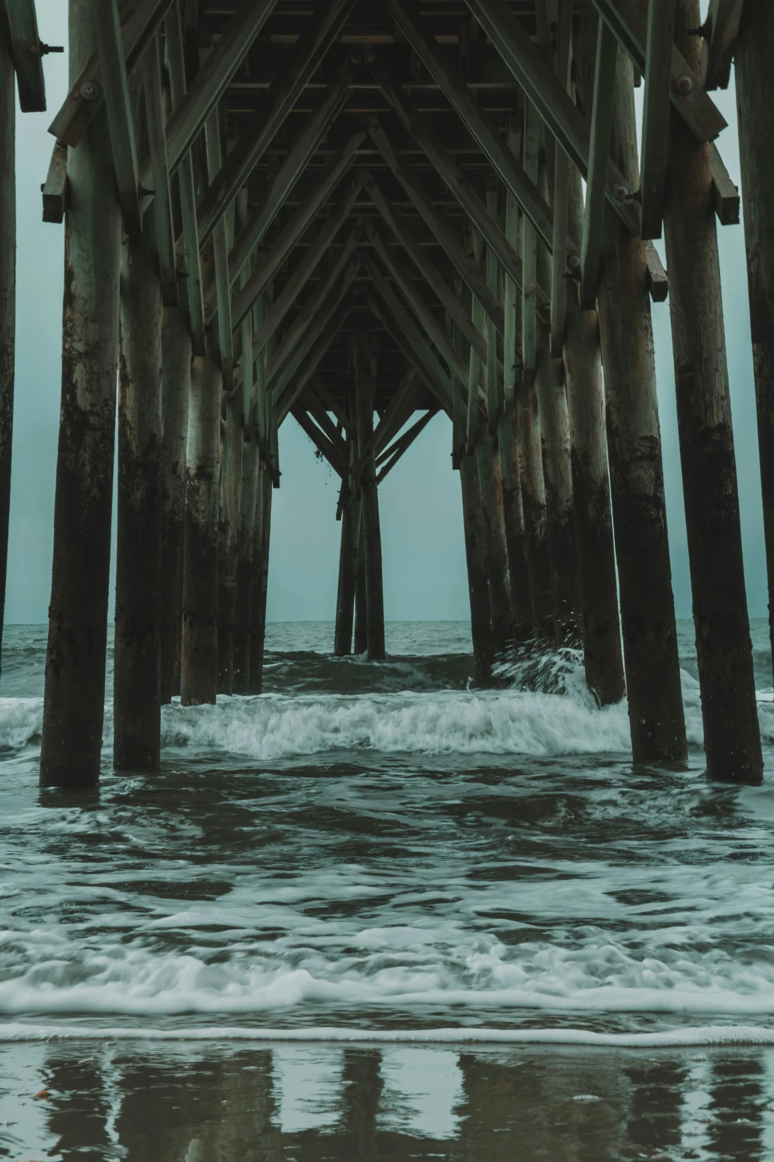 the ocean under a pier at dusk with waves crashing under it