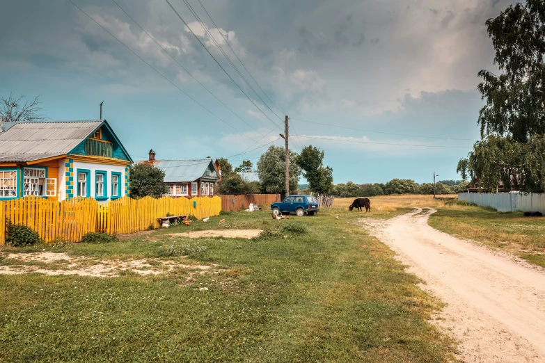 an old yellow barn with blue shutters sitting on the side of a dirt road