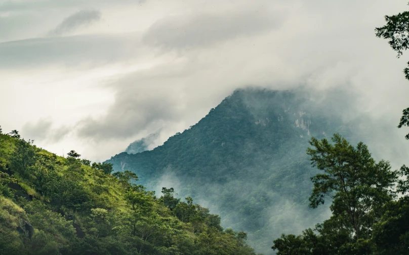 there is clouds coming over a mountain on a cloudy day