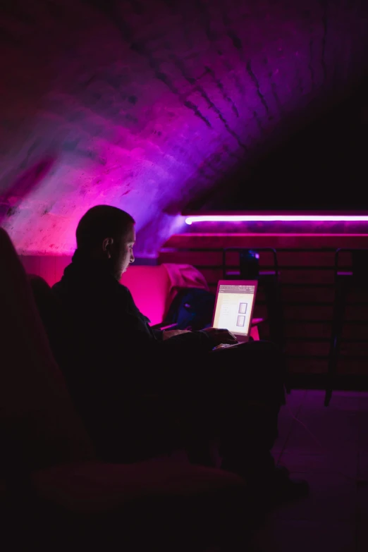 person with laptop in a dark room with light coming through the ceiling