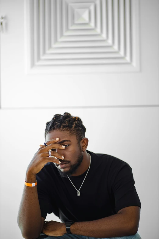 man with hand to face sitting on chair in front of white wall