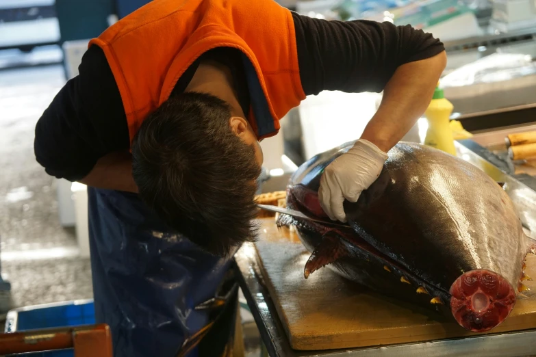 a man with an orange vest is slicing up fish