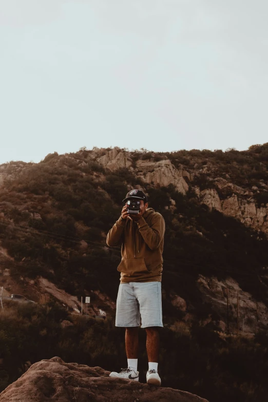 a man taking a selfie on a hill in front of mountains