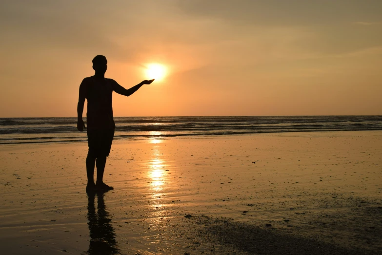 the silhouette of a man standing on a beach at sunset