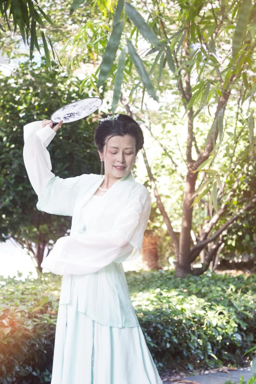 woman in white dress posing outdoors next to trees