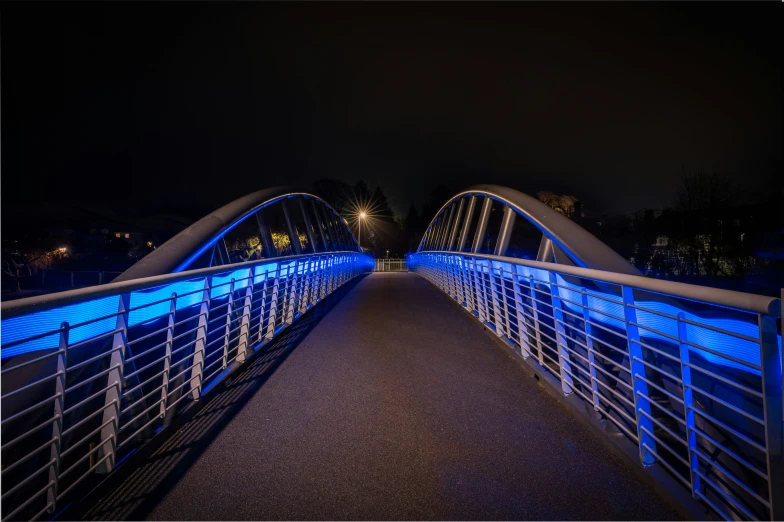 a blue lit pedestrian bridge crosses over a small creek