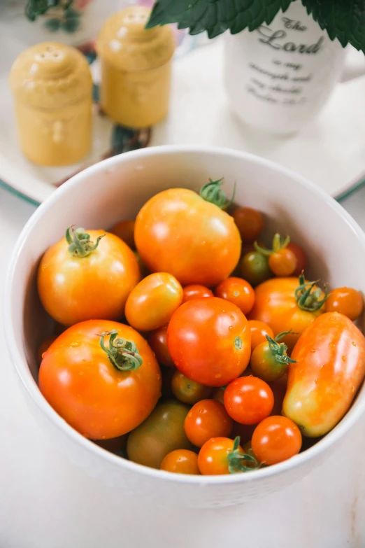 a white bowl full of ripe cherry tomatoes and garnished with green leaves