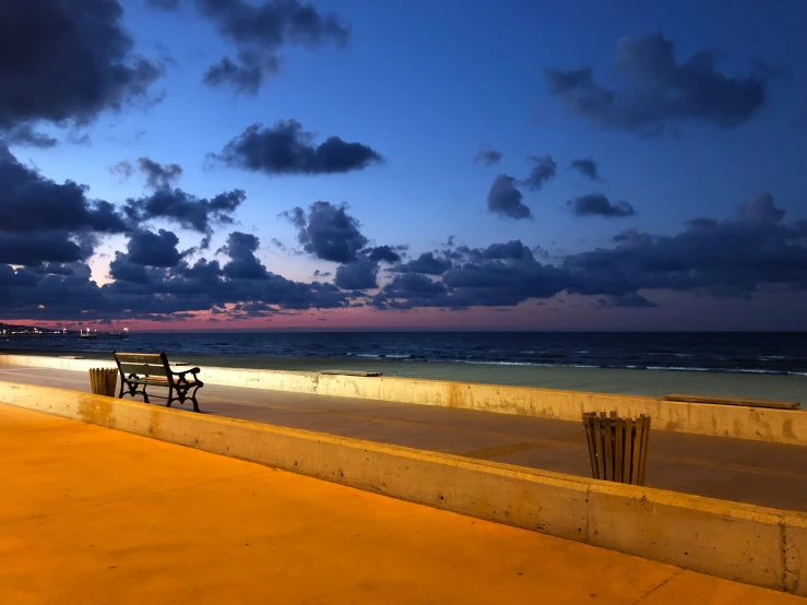 the bench is sitting beside the ocean under a cloudy sky